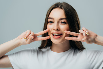 beautiful happy girl showing peace signs near face isolated on grey