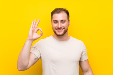 Handsome man over yellow background showing an ok sign with fingers