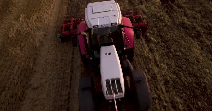 Farmer in tractor cultivating field, aerial view at sunset, front view
