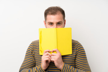 Handsome man over isolated white wall holding and reading a book