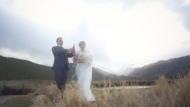 A groom and bride giggle over popping a bottle of champagne at their mountain wedding and then they kiss