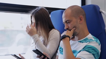 Woman and man traveling by train using their smartphones to spend time on the Internet