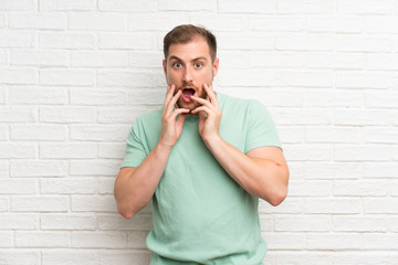 Blonde man over brick wall with surprise facial expression