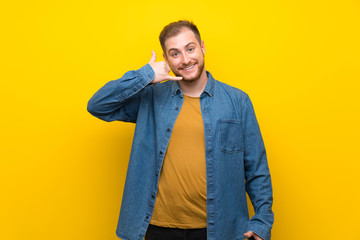 Blonde man over isolated yellow wall making phone gesture. Call me back sign