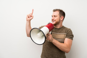 Handsome man over isolated white wall shouting through a megaphone