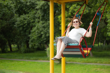 Senior mature woman enjoying retirement life feeling happy and healthy having fun swinging on a swing in the park in a sunny beautiful day.