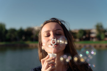 Fototapeta premium Portrait of a young beautiful woman in a dress blowing bubbles