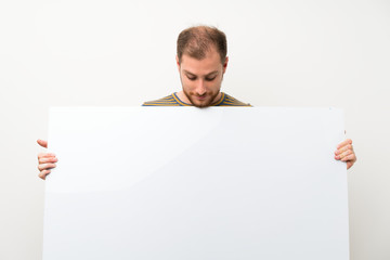 Handsome man over isolated white wall holding an empty white placard for insert a concept