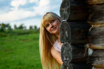 A young girl looks around the corner of a wooden barn. Young long-haired girl looks from behind a wooden shed
