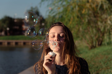 Portrait of a young beautiful woman in a dress blowing bubbles