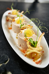 Exquisite Serving White Restaurant Plate with Mousse of Cod Liver, Onion and Crispy Chips Close Up. Stylish Italian Seafood Dish on Natural Dark Stone, Leaves, Flowers and Fruits Background