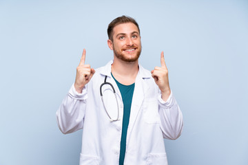 Handsome doctor man over blue wall pointing up a great idea