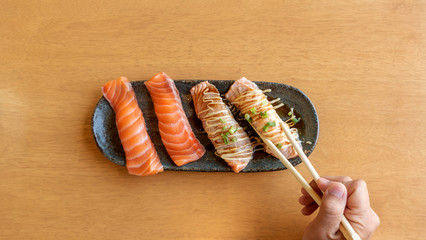 chopsticks tong fresh salmon sushi on a wooden table.