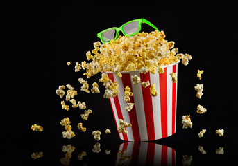 Flying popcorn from striped bucket isolated and 3d glasses on black background