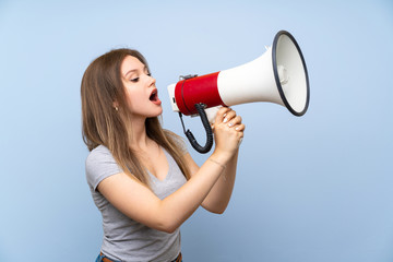 Teenager girl over isolated blue wall shouting through a megaphone
