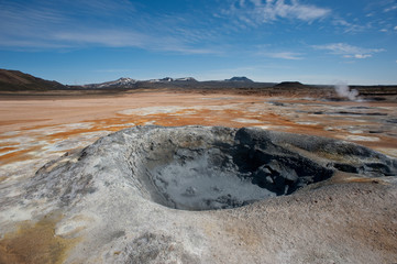 A wide angle view of icelandic volcanic landscape.Mud pot bubbling in foreground and steam vents in distance with volcanic mountains on horizon - Image © Tony Skerl