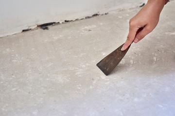 Person with a scraper removes the imperfection from the floor for installing laminate wood. Floor repair inside the room - obrazy, fototapety, plakaty