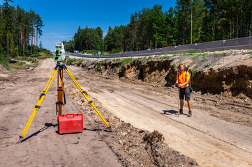 Fototapeta na wymiar Surveyor engineer with equipment (theodolite or total positioning station) on the construction site of the road, highway or building in background