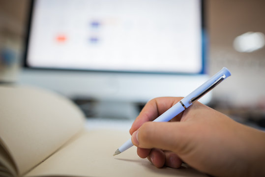 Hombre escribiendo cuaderno, libro con esfero blanco con fondo de pantalla de computador de escritorio