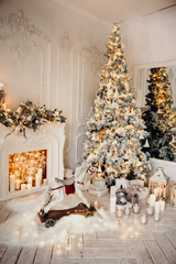 classical luxury interior of a white room with Christmas tree with garland, decorated fireplace, rocking horse, gifts for new year
