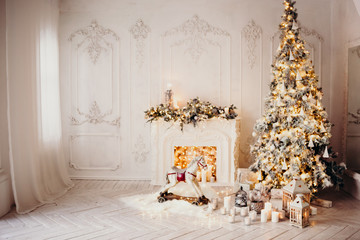 classical luxury interior of a white room with Christmas tree with garland, decorated fireplace, rocking horse, gifts for new year