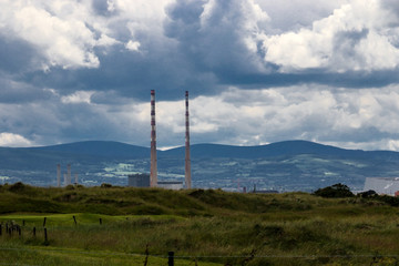 The twin towers of Poolbeg Power Station with the Dublin mountains in the background and the green grass of Bull Island causeway in the foreground.