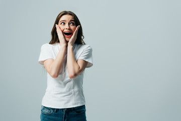 shocked happy beautiful girl in white t-shirt touching face isolated on grey