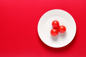 Tomatoes on white plate on red background