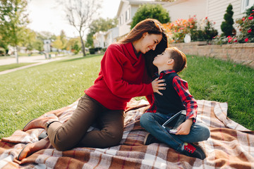 Elegant woman in a autumn park. Family near house. Mother sitting on a plaid with her little son.