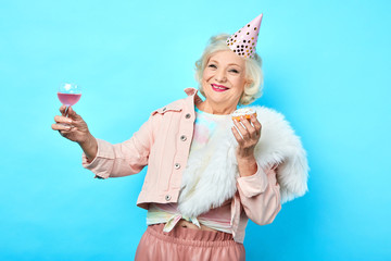 happy positive funny senior woman having fun in the party. isolated blue background. studio shot....