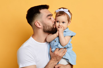 Happy young handsome man holding and kissinga little girl, isolated on yellow. cose up photo....