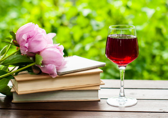 Glass of red wine,  bouquet of flowers and books on  garden background