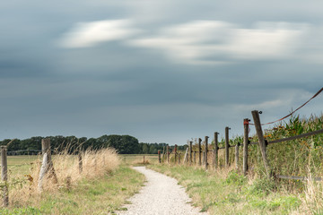 Dirt pathway between fence and corn field under cloudy sky. Long exposure shot.