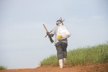 Homem andando pela estrada rural com ferramentas e saco nas costas.