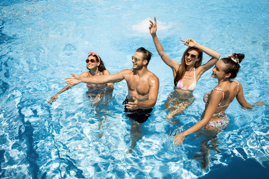 Company of young merry girls and guy are having fun in the swimming pool on the open air on a sunny summer day