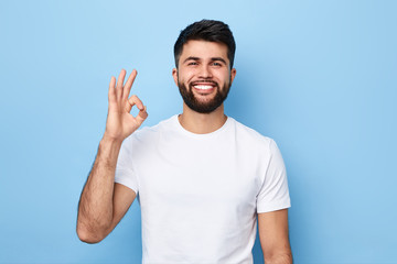 handsome positive bearded man in white T-shirt isolated on blue background showing ok sign.close up...