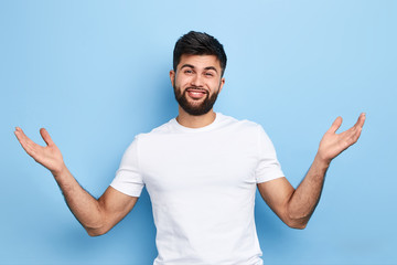 young cheerful handsome man raising his hands with open palms, greeting friends, welcome gesture. isolated on blue background. close up portrait.body language
