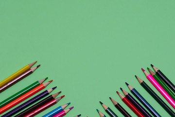 Many colored pencils lie on a green background. Copy spase. The concept of back to school, the educational process, study at school, drawing
