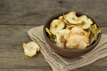 Apple chips in a brown clay bowl on wooden background
