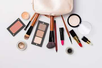 A pink makeup bag with cosmetic beauty products spilling out on to a light  background, with empty space at side