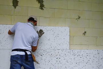 Worker installing white rigid polyurethane foam sheet on aerated concrete block building wall...