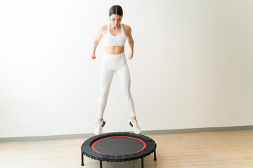 Pretty Young Woman In White Sportswear Jumping On Trampoline