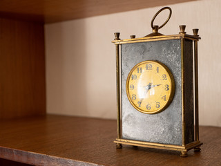 close-up of old vintage table black marble mechanic clock on wooden shelf with golden dial face and metallic circle for moving