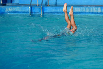 Caucasian boy making jump into swimming pool water. Moment of entrance in water.