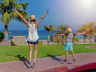 European woman and her son are happy to see the sea. They are jumping against the beach and enjoying their holidays. Back view.