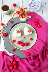 Valentine`s Day breakfast two heart honey cakes on ceramic plate with red fabric and red apples and red flowers on white wooden table,top view,romantic morning food