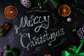 Christmas background with a words:Merry christmas, dry orange,white pinecone,green christmas tree balls,ginger sticks,green ribbon on a black background,flat lay