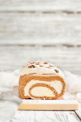 Obraz na płótnie Canvas Beautiful fresh baked pumpkin spice roll cake with powdered sugar, pecans, cream cheese filling and icing. Extreme selective focus with blurred background.