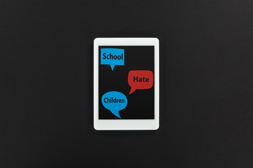 top view of digital tablet and speech bubbles with school, hate and children words on black background, cyberbullying concept