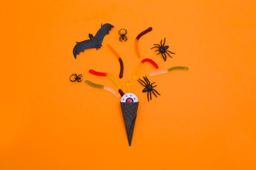Ice cream cone with candy corn and Halloween decorations  on an orange background.